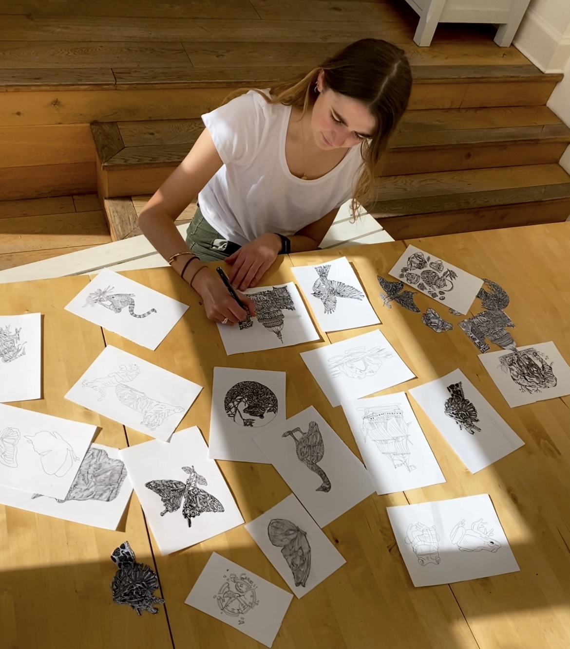 Louisa at a wooden table surrounded by hand drawn ink studies of animals and architecture